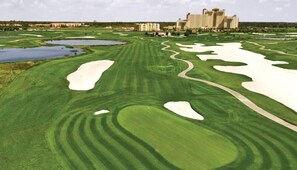 Un parcours de golf avec des bunkers, un obstacle d’eau et un grand hôtel en arrière-plan.