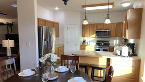 Uma cozinha moderna com armários de madeira, eletrodomésticos de aço inoxidável e um espaço de refeições com uma mesa redonda para quatro pessoas.