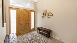 Uma porta de madeira com um painel de vidro, um banco, um tapete estampado e um objeto decorativo fixado na parede.