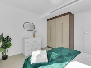 Un dormitorio con cama, cómoda, espejo, armario y una planta en maceta.