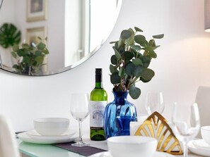 Uma mesa de jantar com uma tigela branca, uma taça de vinho, uma garrafa de vinho e um vaso azul com folhas verdes.