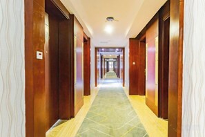 A hotel corridor with wooden doors, a patterned carpet, and a ceiling light. - Shuixi Hotel (Qianxi)