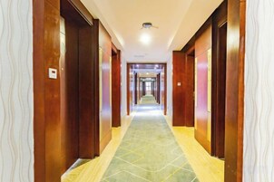 A hotel corridor with wooden doors, a patterned carpet, and a ceiling light.