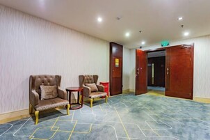 Un hall de hotel con dos sillones, una mesita redonda y una alfombra de diseños geométricos.