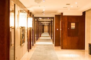 Un pasillo de hotel con un largo corredor, puertas de madera y lámparas de pared.