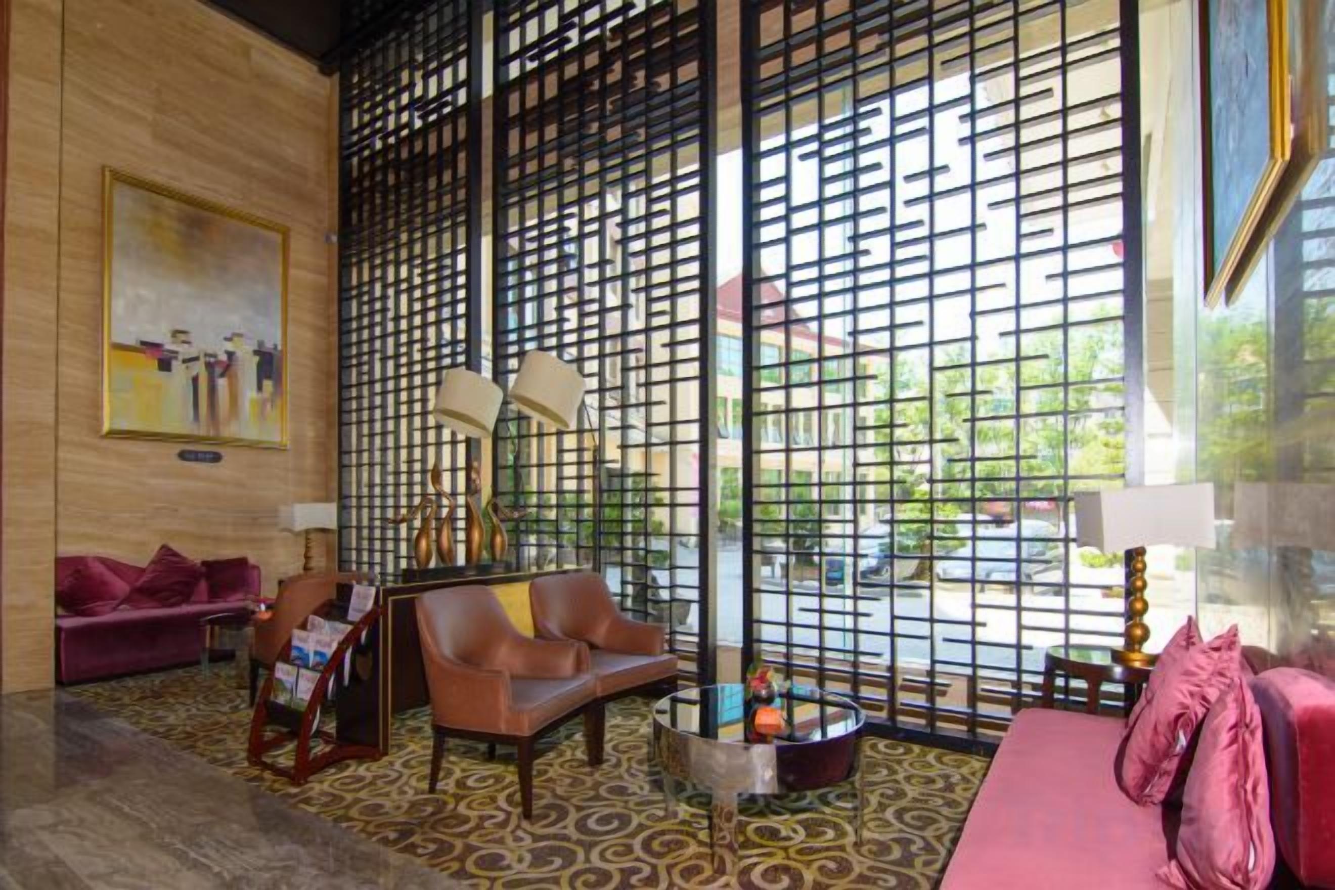 A room with a patterned floor, a sofa, a chair, a table with a lamp, and a decorative partition.