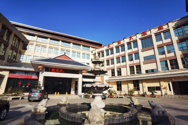 A hotel entrance with a fountain, multiple floors, and a clear sky.