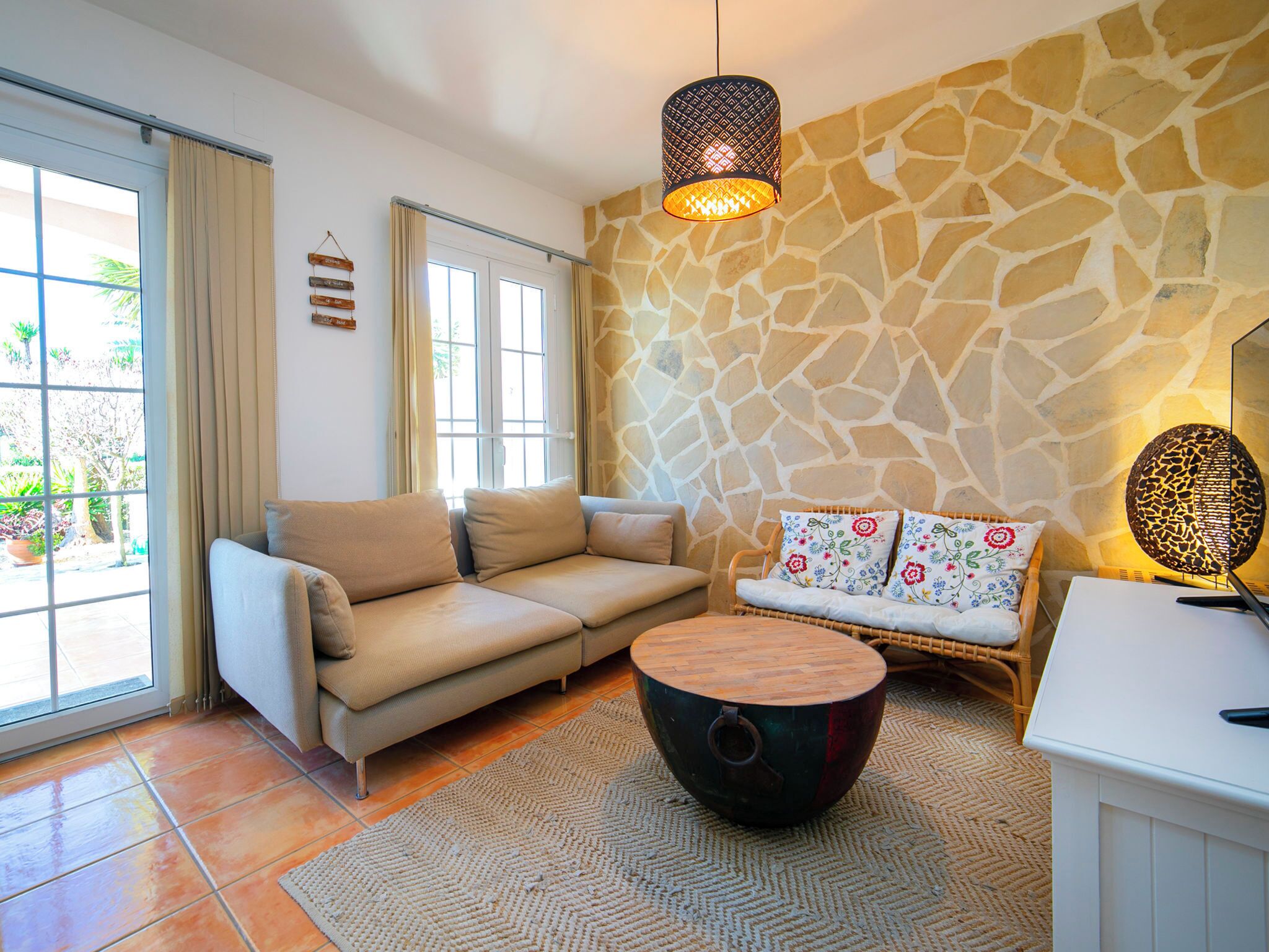A living room with a stone wall, a beige sofa, a round coffee table, and a hanging light fixture.