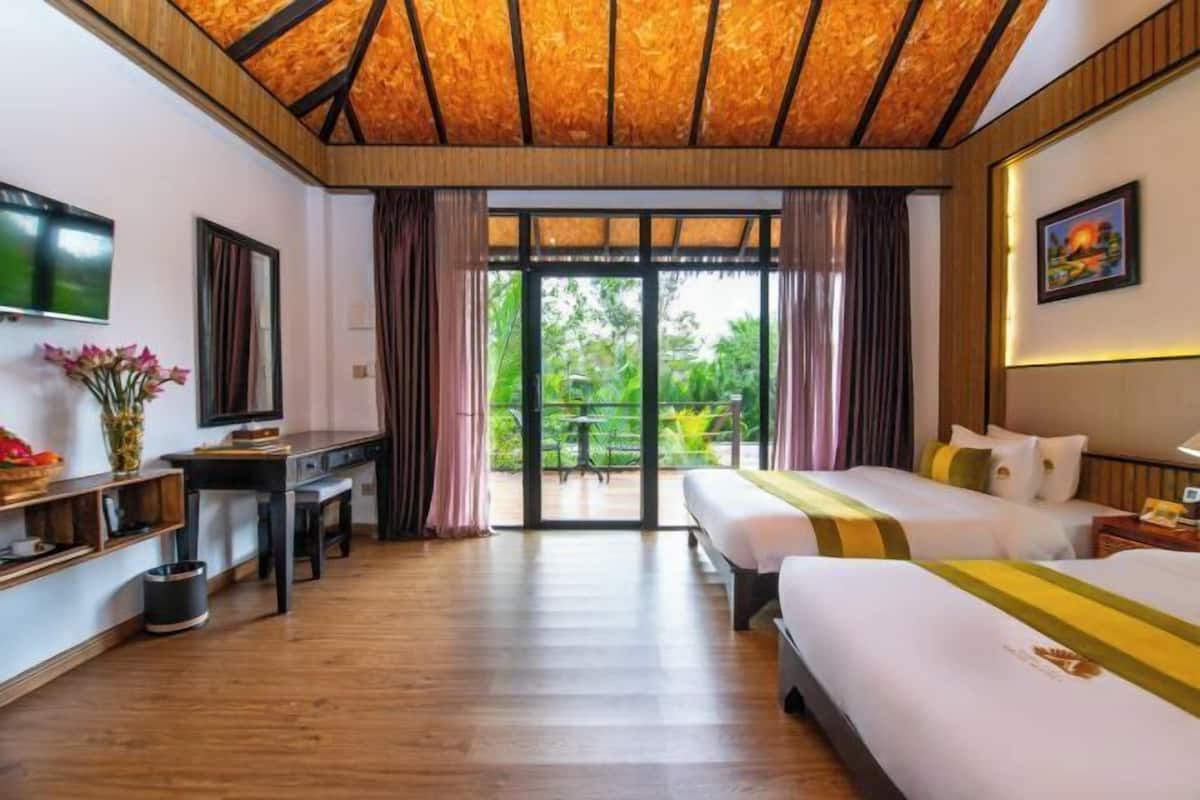 Une chambre d’hôtel avec un plafond en bois, un lit, un bureau, une télévision et une vue sur la verdure.