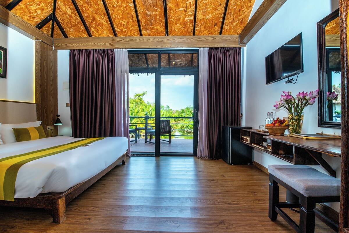 Une chambre d’hôtel avec un grand lit, un bureau, une télévision et un balcon donnant sur un espace verdoyant.