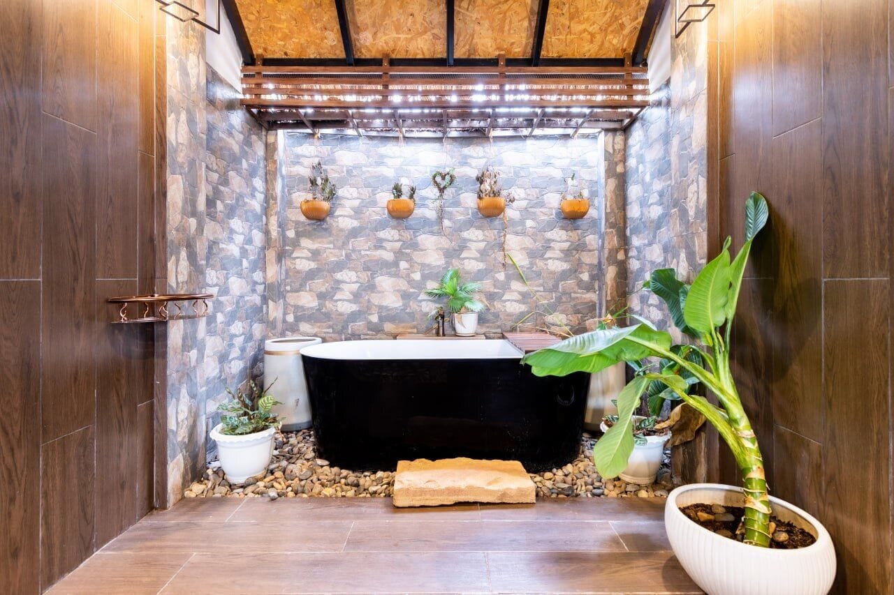A bathroom with a stone wall, a bathtub, and several potted plants.