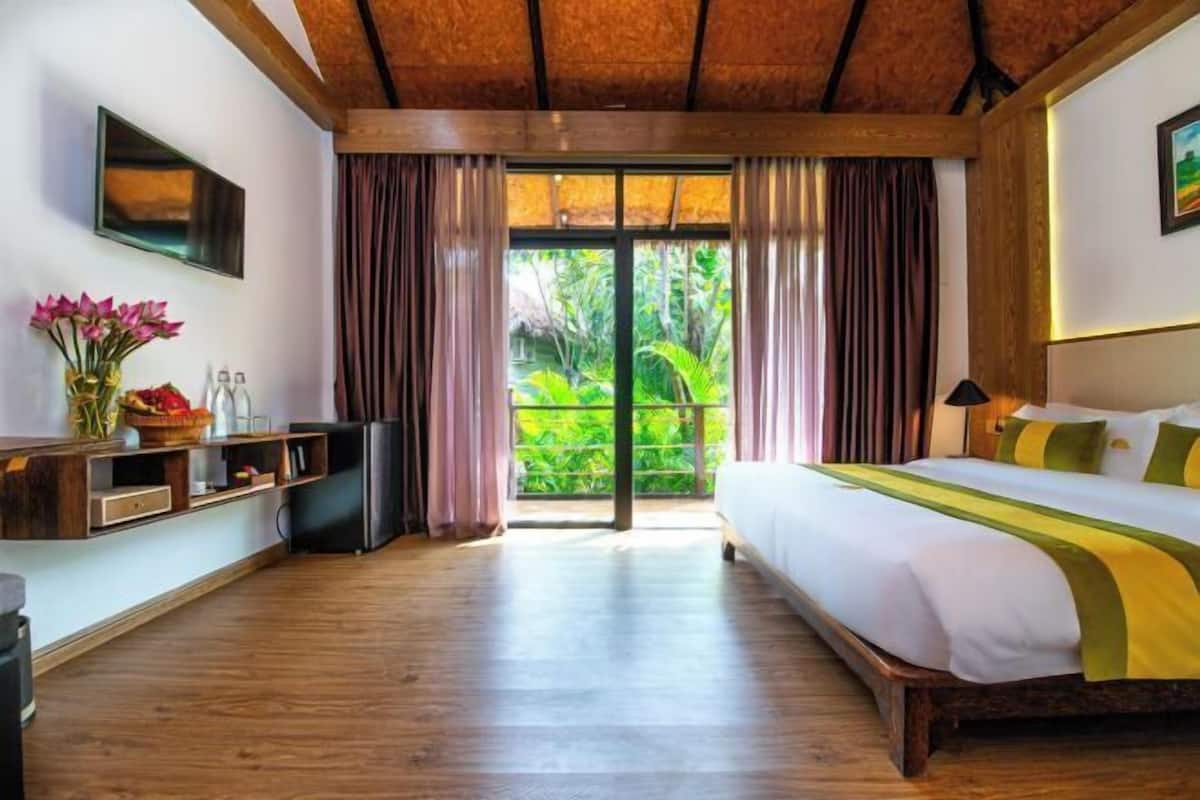 Une chambre d’hôtel avec un lit, un bureau, une télévision et une vue sur la verdure par la fenêtre.