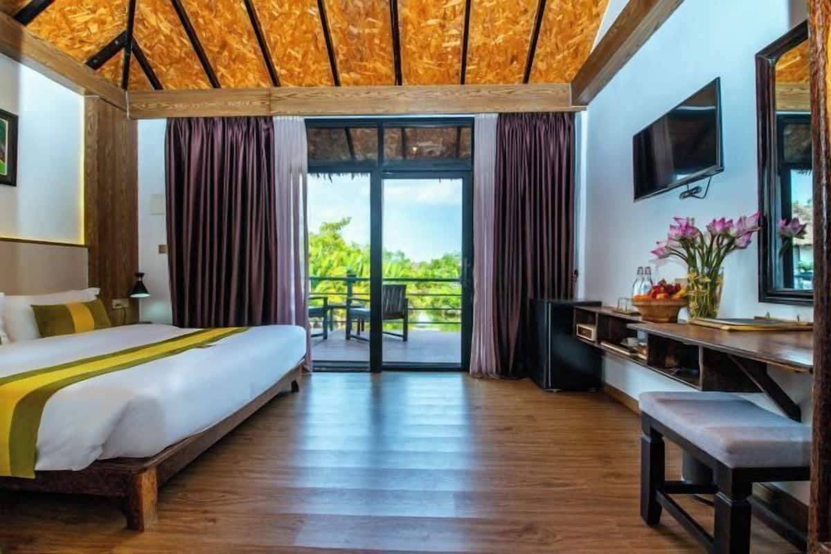 Une chambre à coucher comprenant un lit, un bureau, une télévision et un balcon avec des rideaux.