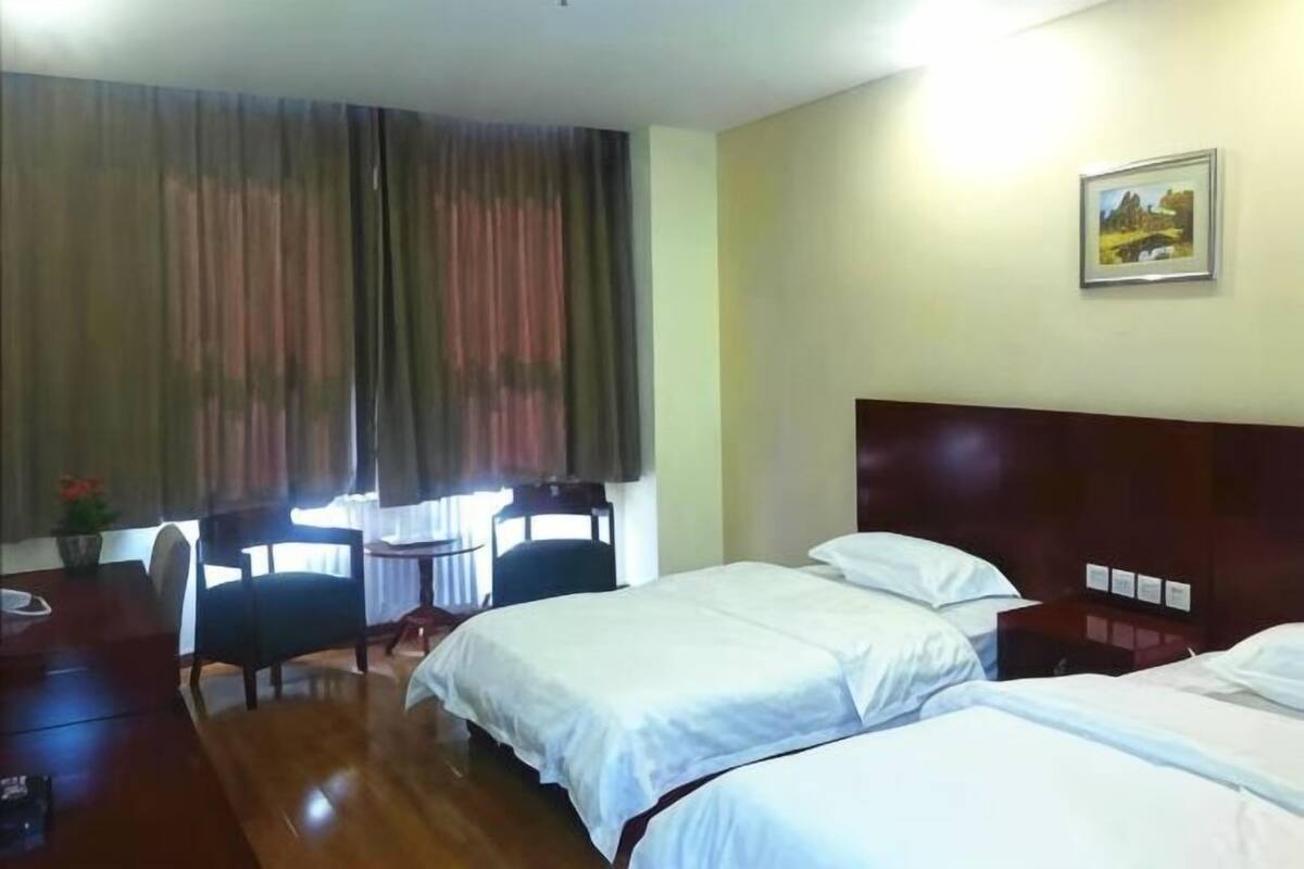 Une chambre d’hôtel avec deux lits, un bureau en bois, une chaise et une fenêtre avec des rideaux.