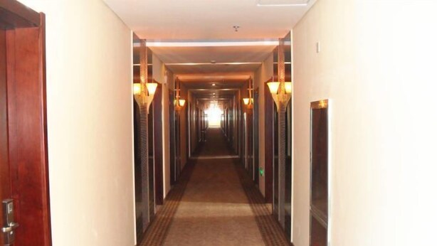 Een hotelgang met een vloerbedekking, houten deuren en wandlampen.