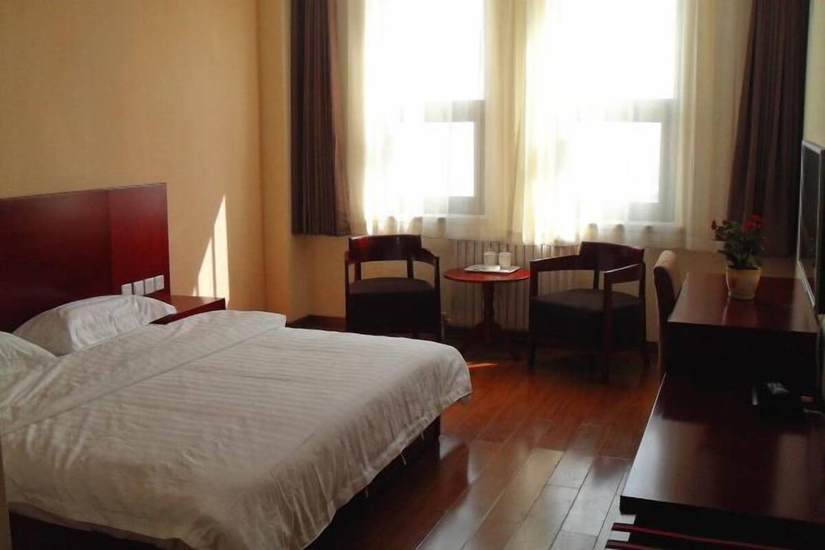 Une chambre d’hôtel avec un lit, un bureau, deux chaises, une petite table et une fenêtre avec des rideaux.