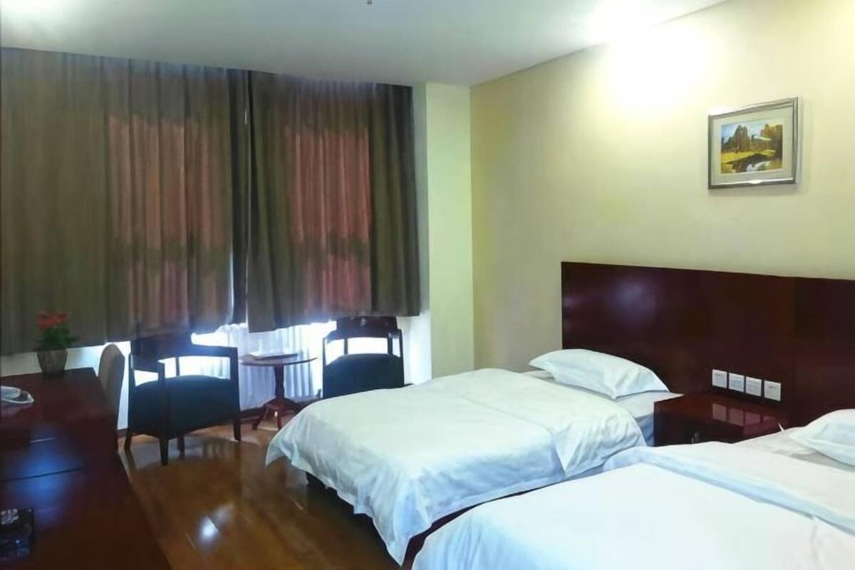 Une chambre d’hôtel avec deux lits, un bureau, une chaise et une fenêtre avec des rideaux.