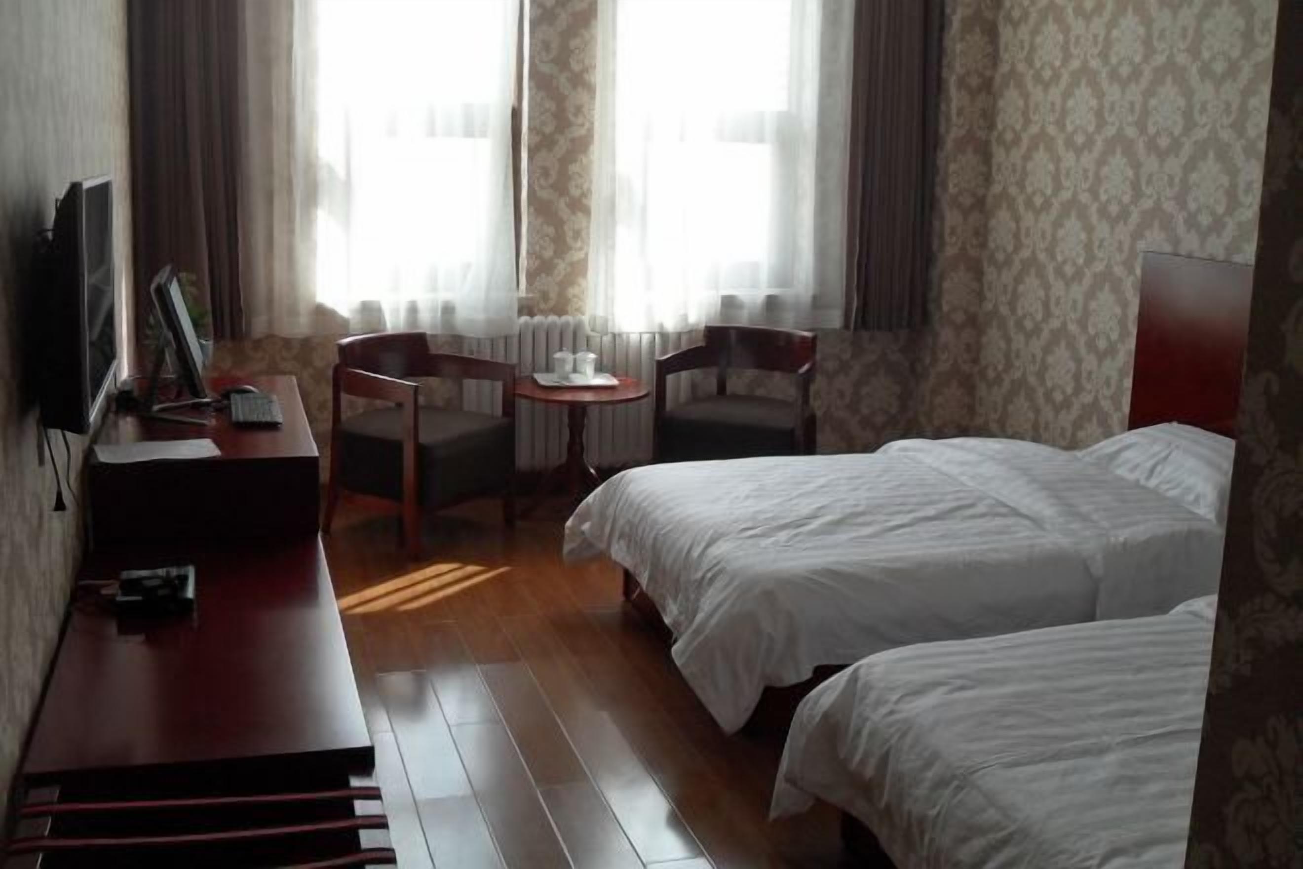 A hotel room with two beds, a desk with a computer, a chair, and a small table with cups.
