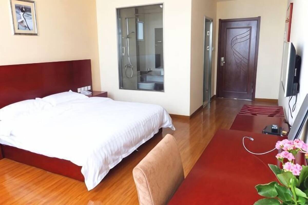 Une chambre d’hôtel avec un lit, une télévision, une moquette rouge et une fenêtre donnant sur une salle de bain.
