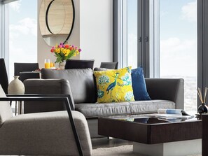 Un salon moderne avec un canapé gris, une table basse et une vue sur la ville grâce à de grandes fenêtres.