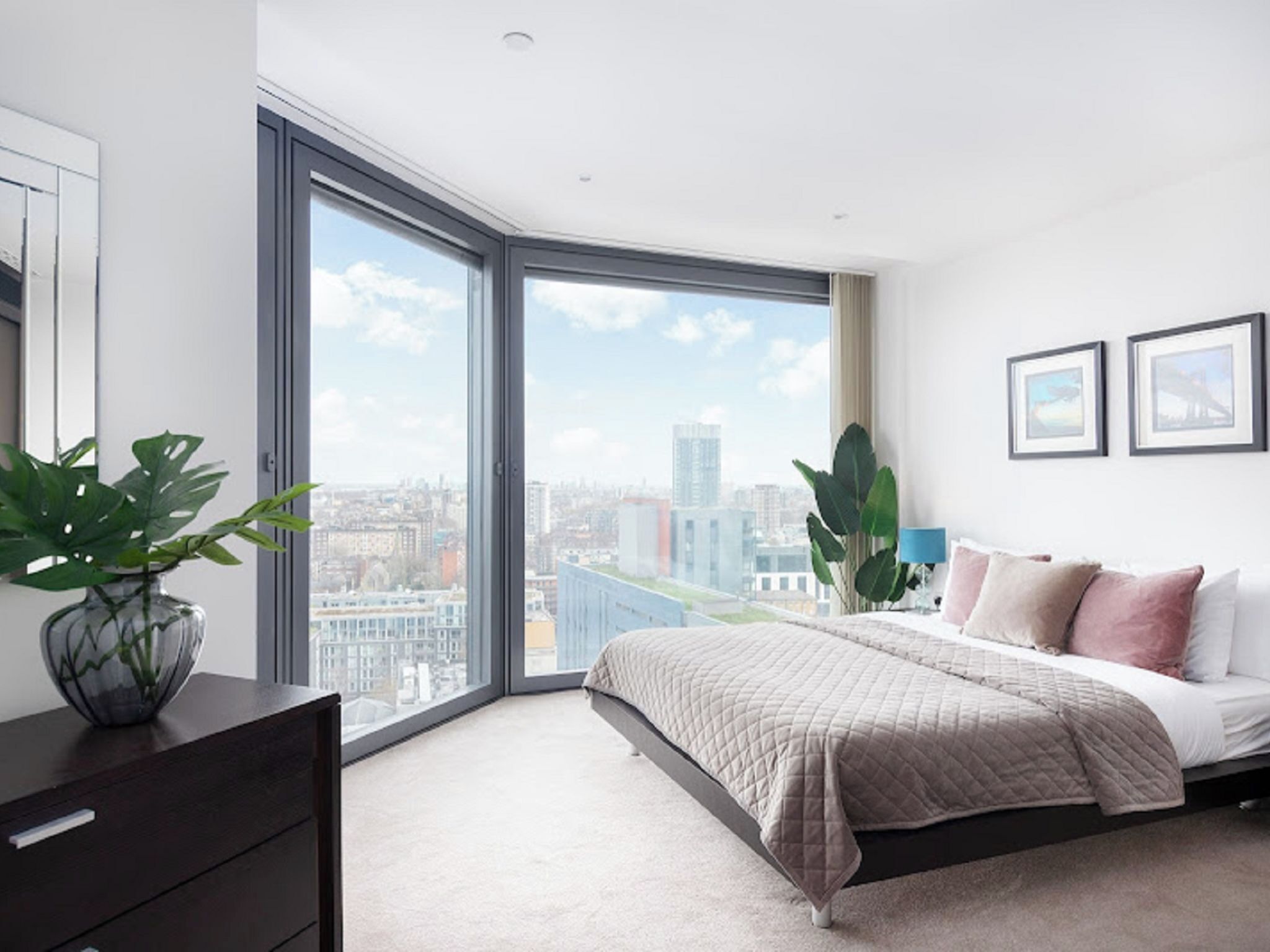 Ein modernes Schlafzimmer mit großem Fenster, einem Bett, einer Kommode und Blick auf die Stadt.