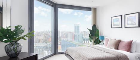 Un dormitorio moderno con una ventana grande, una cama, un aparador y vistas a la ciudad.