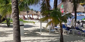 Een strand met rieten hutten, palmbomen en strandstoelen.