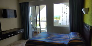 Hotelkamer met een bed, een televisie, een bureau en uitzicht op een gebouw en een balkon.