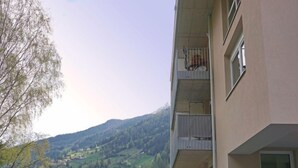 Ein mehrstöckiges Gebäude mit Balkon, Blick auf eine gebirgige Landschaft und einer eingezäunten Grünfläche.