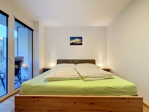 A bedroom with a bed, a nightstand, a lamp, and a window.