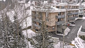 Ein mehrgeschossiges Gebäude mit Balkonen, umgeben von schneebedeckten Bäumen und einer Bergkulisse.