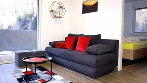 Ein modernes Wohnzimmer mit einem grauen Sofa, roten Kissen, einer geometrischen Wanddekoration und einem Gemälde vom Sonnenuntergang.