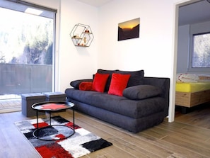 Ein modernes Wohnzimmer mit einem grauen Sofa, roten Kissen, einer geometrischen Wanddekoration und einem Gemälde vom Sonnenuntergang.