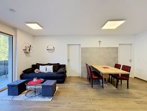 A modern living room with a black sofa, a coffee table, and a dining area with a wooden table and red chairs.