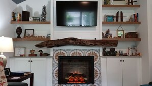 Ein Wohnzimmer mit Kamin, Fernseher darüber und Regalen mit Büchern und Dekoration.