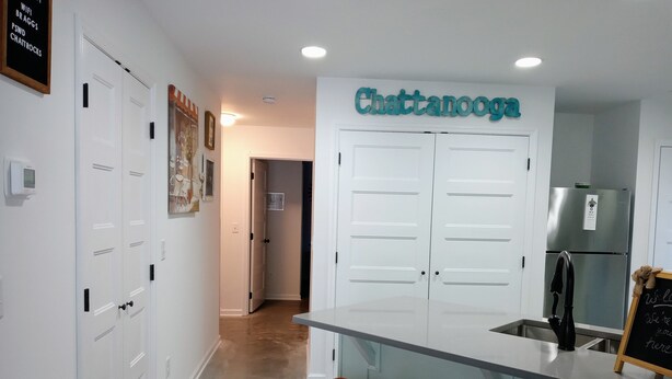 Eine moderne Küche mit einem 'Chattanooga'-Schild, weißen Schränken, einem Edelstahlkühlschrank und orangefarbenen Barhocker.