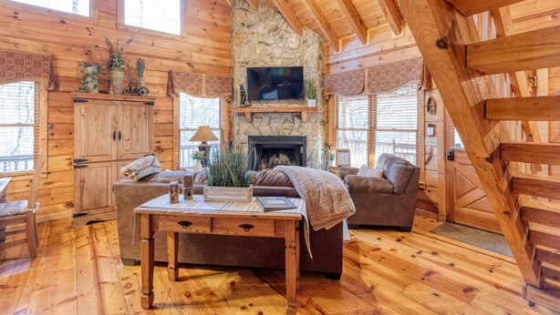Un intérieur chaleureux de chalet en bois, avec une cheminée en pierre, des meubles en bois et de grandes fenêtres.
