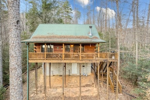 A log cabin with a green roof, a deck, and a staircase leading to a second level.