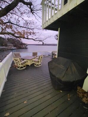 Une terrasse en bois avec des meubles d’extérieur, un barbecue abrité et une vue sur un plan d’eau.