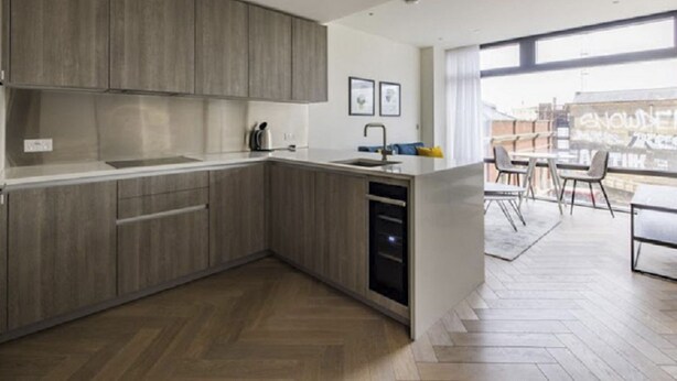 A modern kitchen with wooden cabinets, a built-in oven, and a large window overlooking a cityscape. - Liverpool Street, Shoreditch by Interhome (Shoreditch)