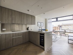 Une cuisine moderne avec des meubles en bois, un four encastré et une grande fenêtre donnant sur un paysage urbain.