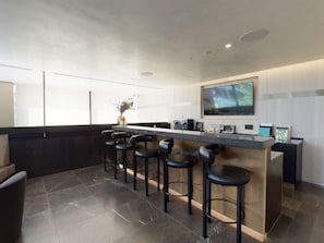 Une cuisine moderne dotée d’un coin bar, comprenant un grand téléviseur, des tabourets de bar et un vase rempli de fleurs.