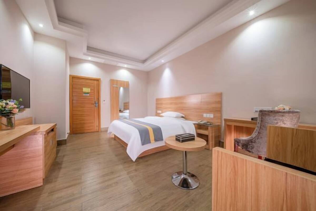 A hotel room with a bed, a desk, a chair, a round table, and a TV.