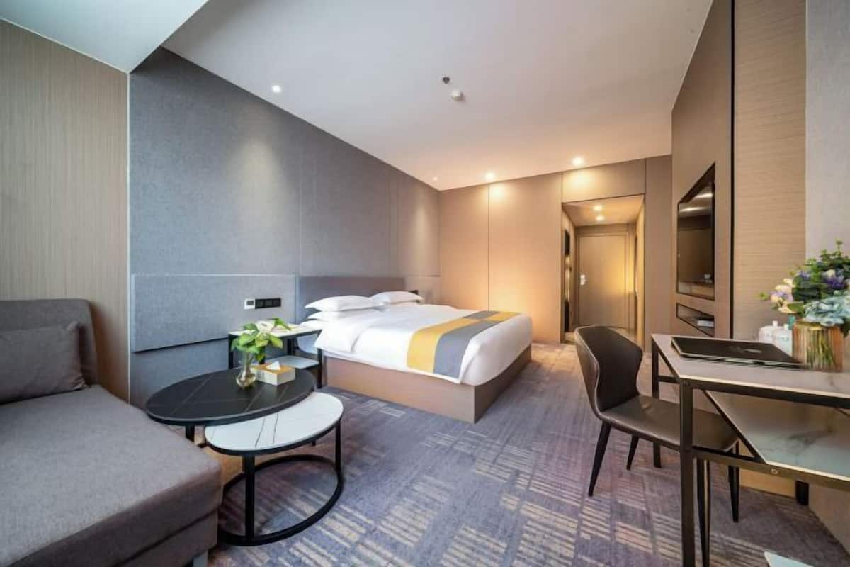 A modern hotel room with a bed, a desk, a chair, and a sofa.