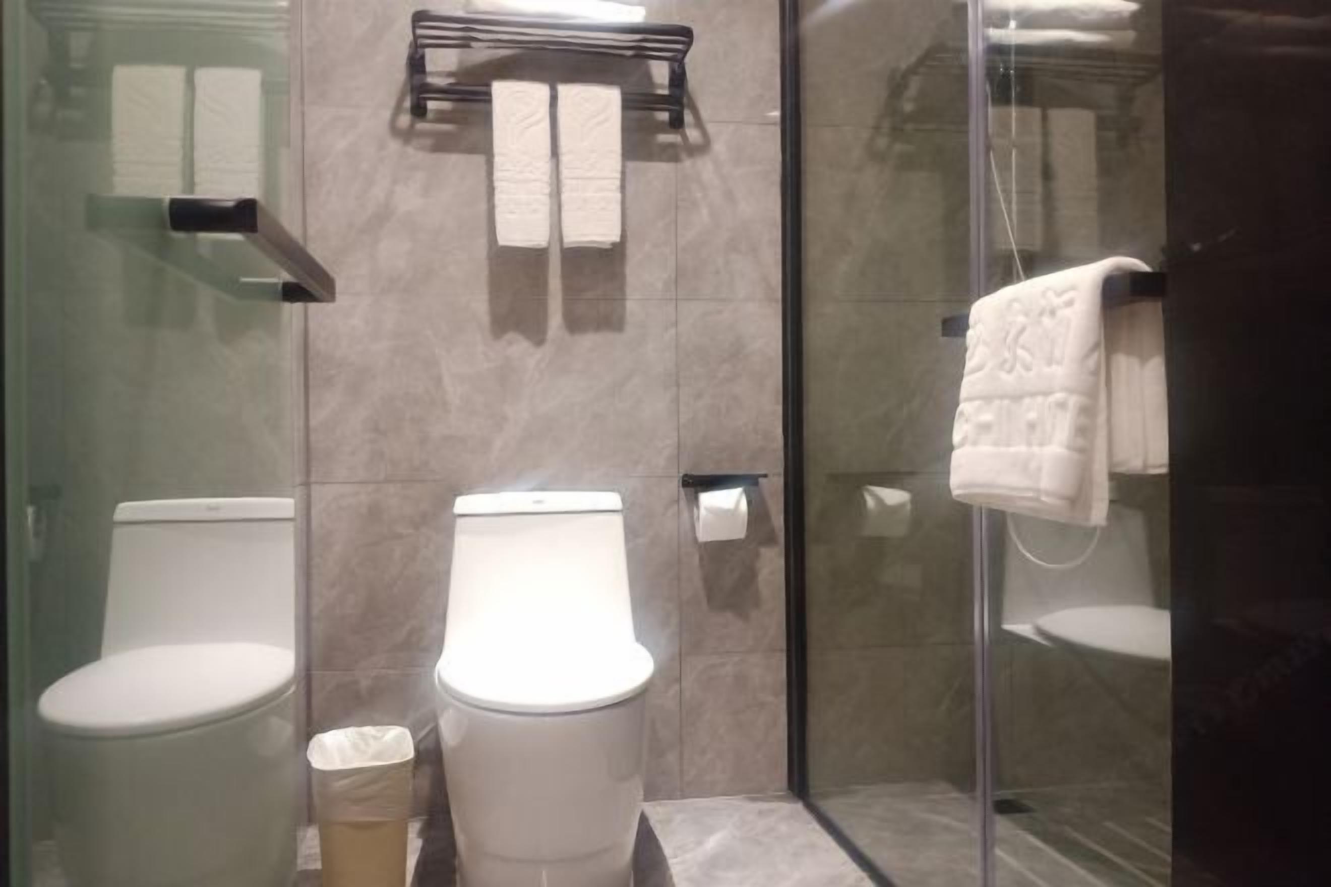 Un baño moderno con dos inodoros, cabina de ducha de vidrio y toallero con toallas blancas.