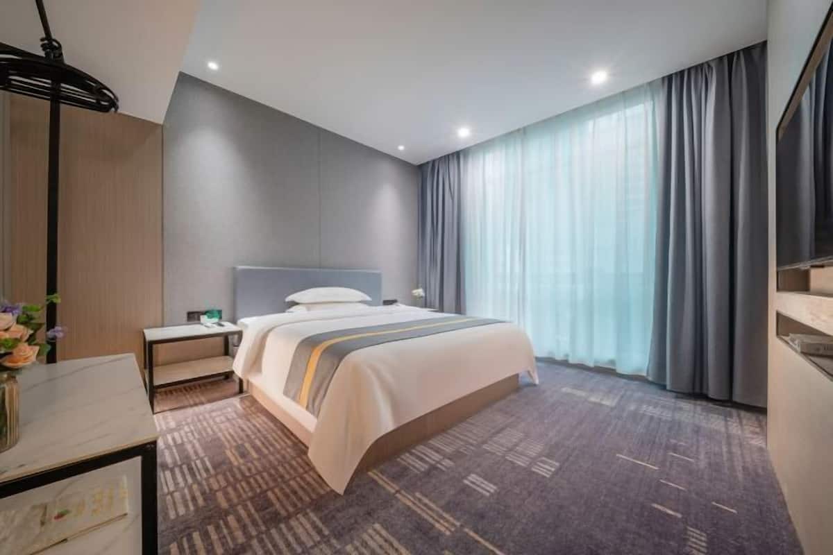 A modern hotel room with a bed, nightstand, and a large window with curtains.
