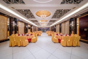 Un salón de banquetes con filas de mesas y sillas, una araña de cristal y paredes de mármol.