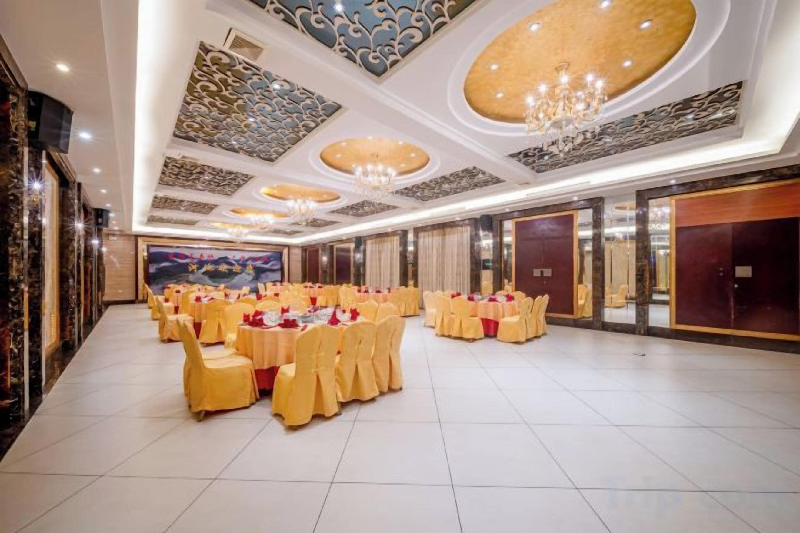 A banquet hall with round tables, chandeliers, and a large mural.