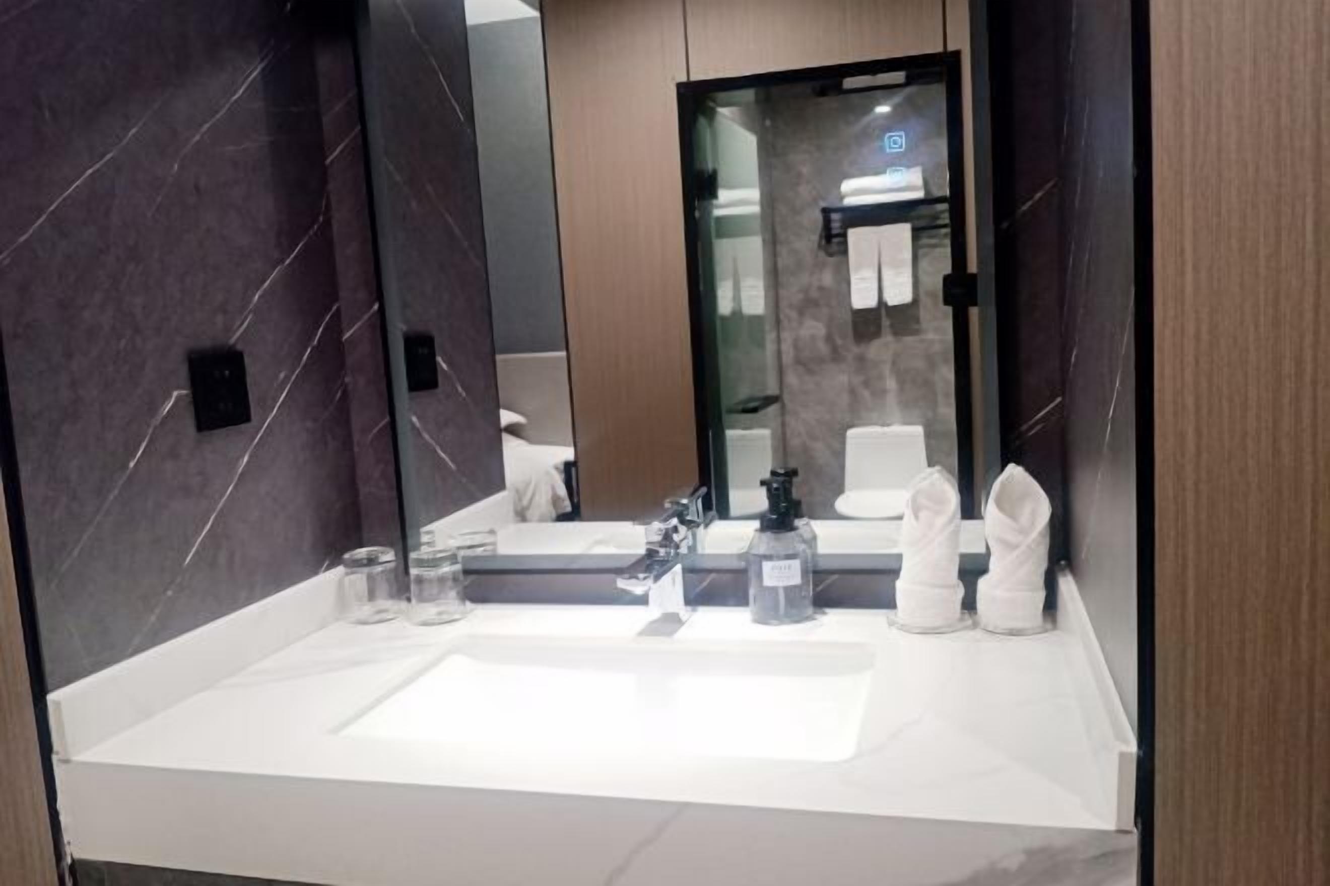 Un baño moderno con un lavamanos blanco, un espejo grande y un separador de vidrio.