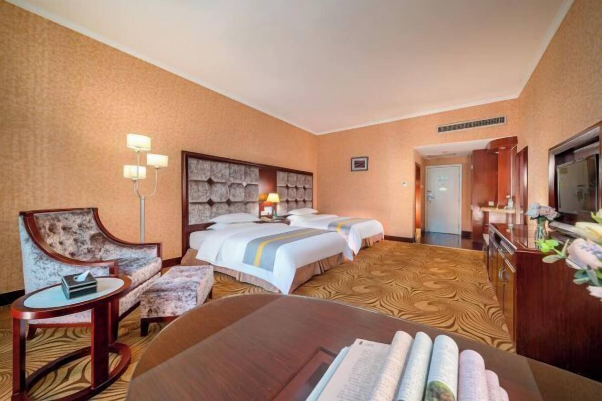 A hotel room with two beds, a sofa, a desk, a lamp, and a television.